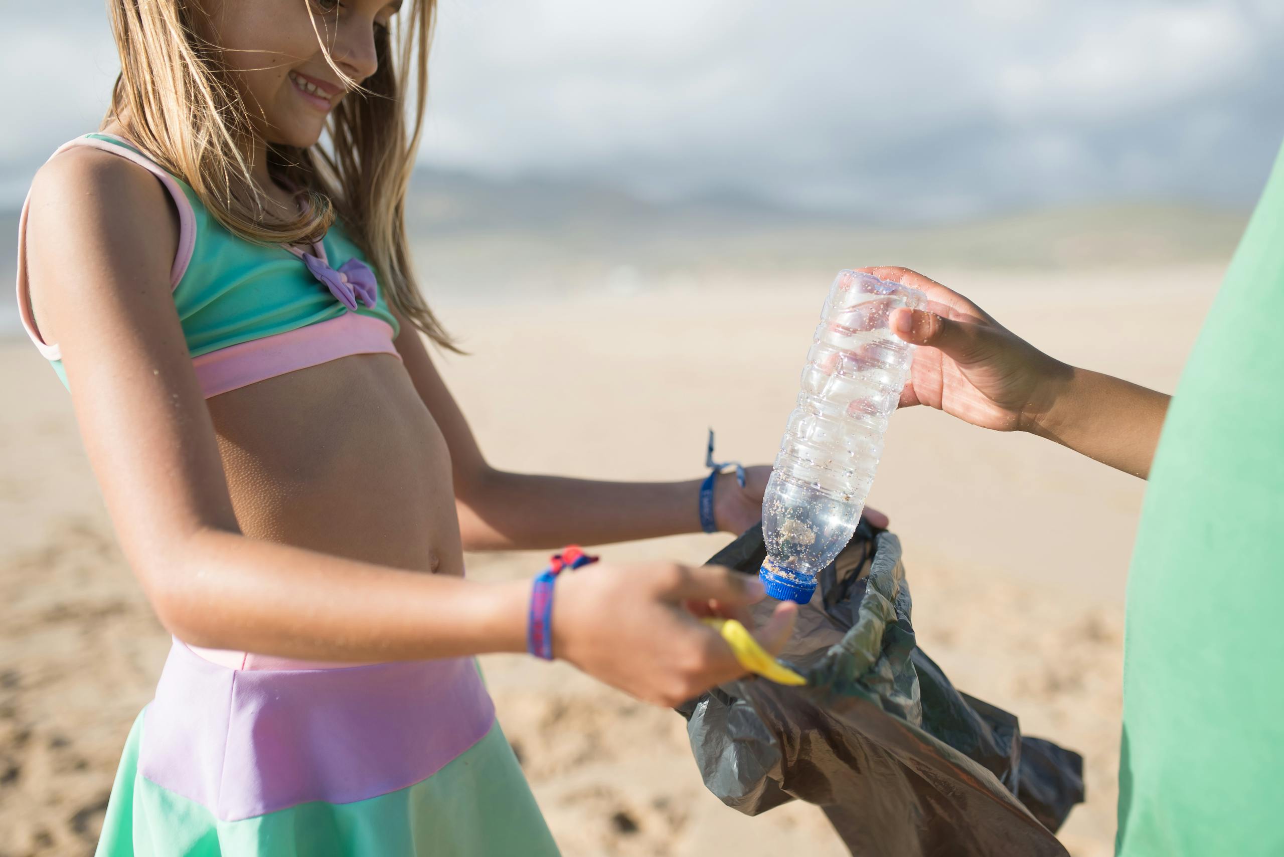 Kids collecting plastic bottles on a sunny beach day, promoting environmental awareness.